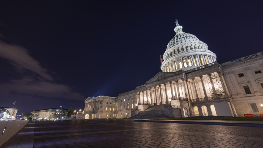 A nighttime time-lapse of the east side of the United States Capitol Building in Washington, DC. Clouds and a few stars are seen in the sky. The ultra-wide shot pans from left to right. Late autumn. Royalty-Free Stock Footage #1096965977