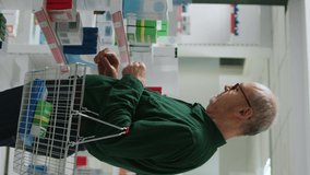 Vertical video: Senior customer smiling and looking at cardiology pills box in pharmacy, preparing to buy prescription medicine and pharmaceutical products. Checking supplements and medication on