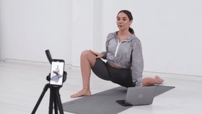 Athletic woman fitness trainer conducts workout online by filming video on a mobile phone. Remote learning and training. Remote business concept.