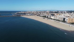 Drone footage of the coast of Porto with a large sandy beach in the foreground. The piers of DocaPesca - Lota de Matosinhos go far from the coast.