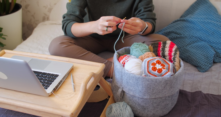 Close-up video of woman learning to crochet. Felt basket with balls of yarn. Anti-stress hobby. Online lessons for amateurs on laptop.