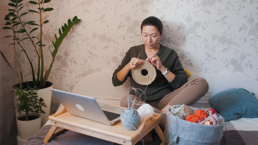 Close-up video of woman learning to crochet. Felt basket with balls of yarn. Anti-stress hobby. Online lessons for amateurs on laptop.