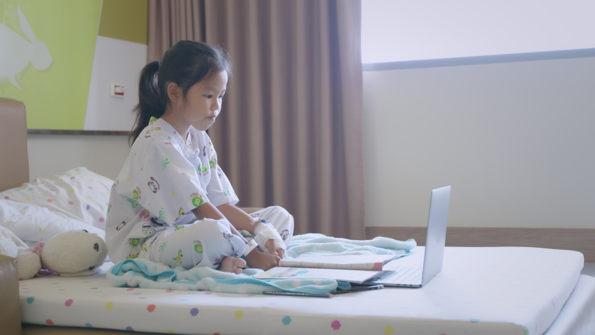 Sick asian child learning online class with teacher and friend at hospital. Sick kid wave her hand to say hi while studying online video call in classroom when stay in hospital. Slow motion shot. Royalty-Free Stock Footage #1096979569
