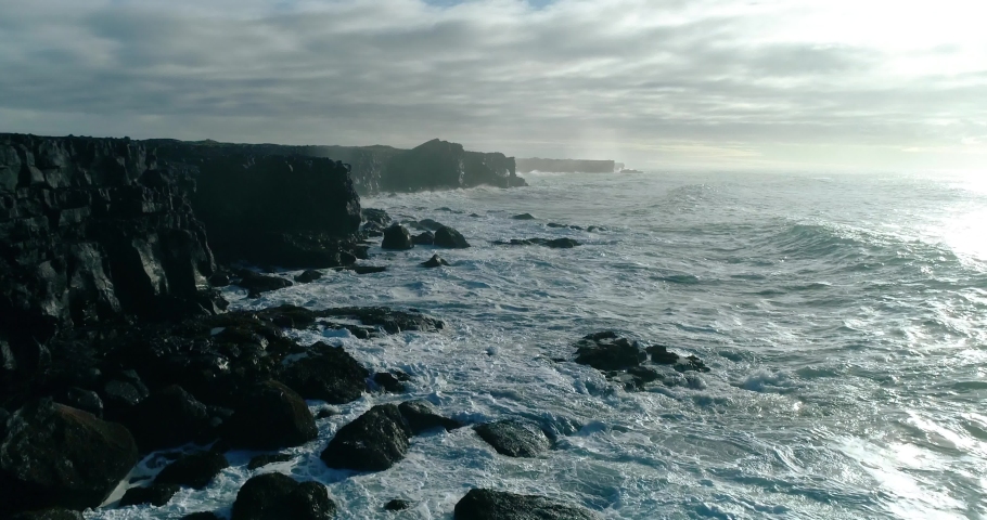 A stormy wave hits a large shore of volcanic black stone. A large wave splashes on a black volcanic rocky cliff in Iceland. the fast wave hits the shore and creates lots of white foam Royalty-Free Stock Footage #1096984027