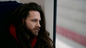 Portrait of a guy with a beard looking out the window on a city transport train. Close-up of a young serious man with dreadlocks