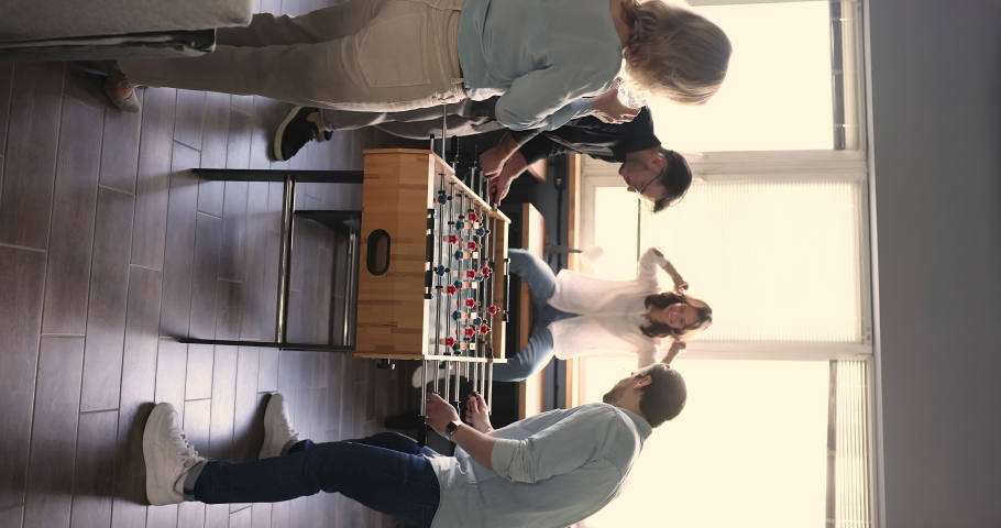 Cheerful employees playing table foosball during break indoors, vertical shot. Workmates cheering, celebrate win, giving high five gesture feel happy enjoy rest at workplace. Friendship, office games Royalty-Free Stock Footage #1096987835