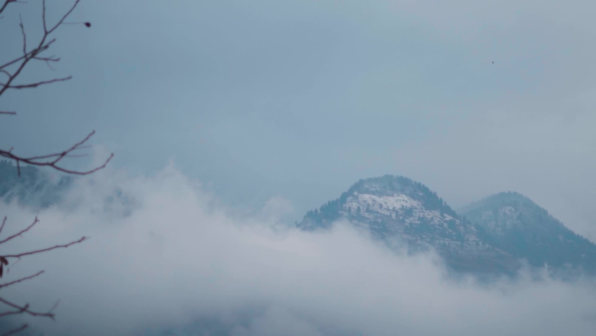 Clouds below the snow covered Himalayan mountains during the snow storm at Manali in Himachal Pradesh, India. Clouds cover the mountain during the storm. Winter background of snowfall in mountains.  | Shutterstock HD Video #1096988649