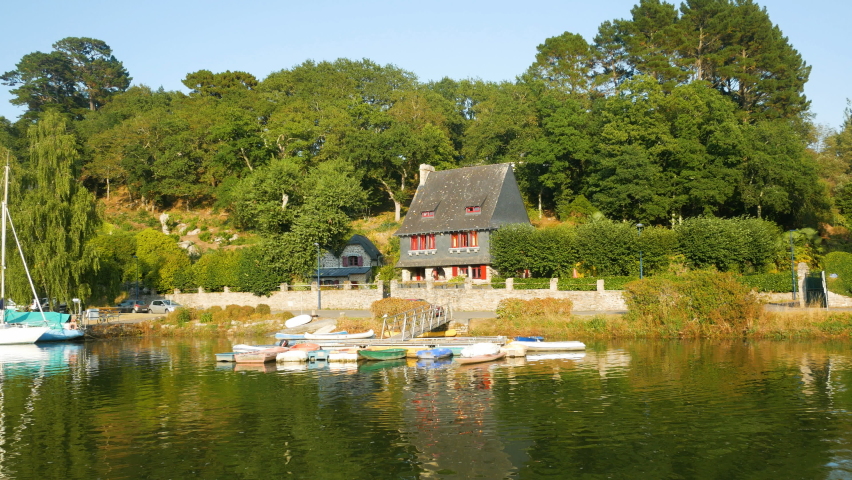 Elegant villa close to the river named "Aven" in the village of Pont Aven, Brittany, France. Several boats on the calm waters during sunset. Blue sky on the background.