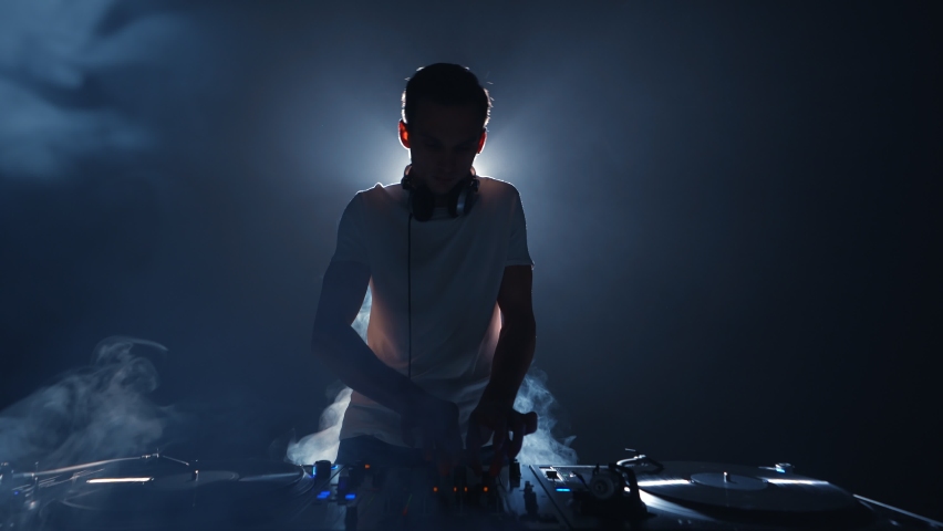 Silhouette of DJ playing music on party in night club. Disc jokey performing in smoke on stage Royalty-Free Stock Footage #1096992857