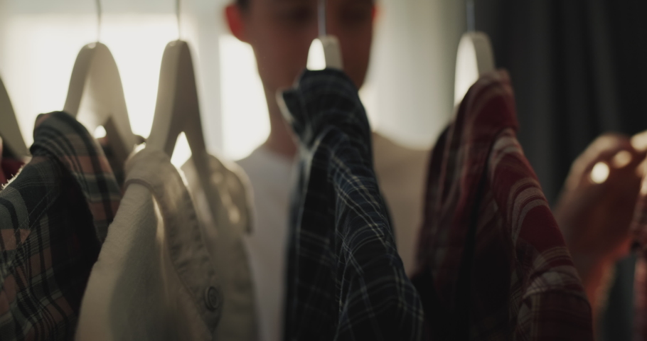 A young man stands at the closet with clothes, chooses a shirt for himself Royalty-Free Stock Footage #1096995561