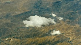 View from plane flying above clouds over green mountains range. Beautiful top view of the green ridges of the mountains. The concept of aerial video filming of landscapes of the earth's surface