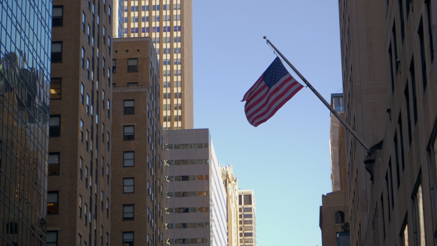 City of New York. View of the American flag on the flagpole on wall of the building and fluttering in the wind. The American flag waving in the wind against the backdrop of tall buildings of New York.