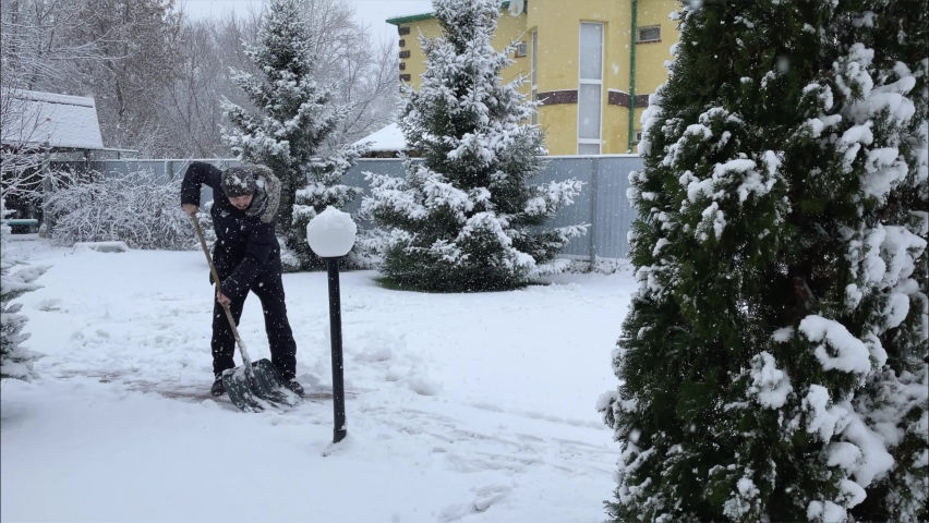 Man cleans the path from snow with a shovel. Next to the Christmas tree in the snow. High quality 4k footage with slow motion Royalty-Free Stock Footage #1097002077