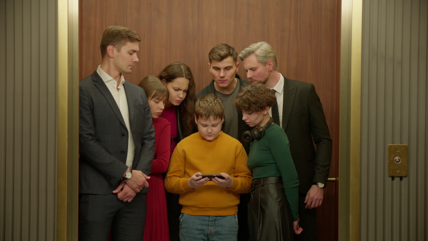 ZOOM IN Surprised Kid boy is using his smartphone in the elevator, everybody watching the screen Royalty-Free Stock Footage #1097004131