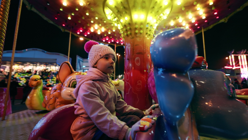 Cute little girl is on a merry-go-round carousel in the amusement park at night Royalty-Free Stock Footage #1097004847