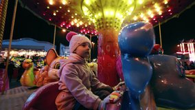 Cute little girl is on a merry-go-round carousel in the amusement park at night