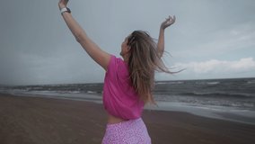 Dark and stormy: Young woman with long legs and in a pink skirt is running along the sea