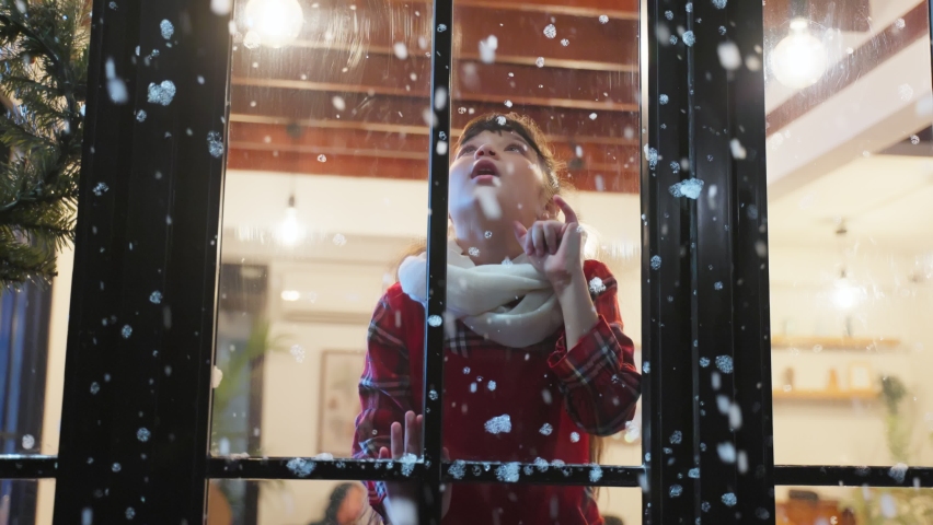 Adorable child look through the window and admiring first snow flakes. Young kid girl sitting in living room at home, watching snow falling outside enjoy celebrate Christmas, Thanksgiving with family.