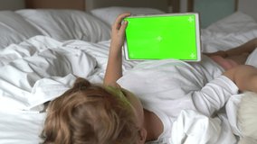 Cute child girl and her favorite pet dog golden retriever watching video cartoons or playing game on wireless digital tablet in white parent bed in bedroom at home. Bonding and relationship pets.