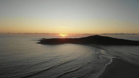 Drone video flying toward Shark Island, Final Bay, as the sun rises behind it. Port Stephens lighthouse silhouetted against the bright sky.