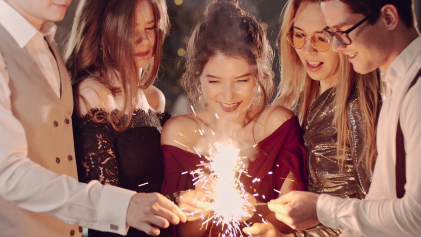 Beautiful friends holding christmas sparklers in hands. Guys celebrating by waving fireworks, enjoying party on New Years or Christmas Eve night. Happy group of people enjoying party in Xmas evening. Royalty-Free Stock Footage #1097020751