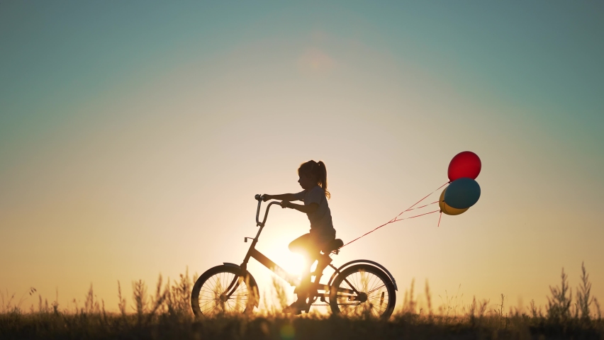 Dream kid. Silhouette of kid on bike in park. Girl rides in park on green grass. Child games in nature.Traveling with balloons on bike.Active child freedom in summer.Girl learns to ride bike in nature Royalty-Free Stock Footage #1097020865
