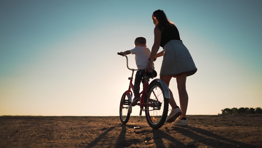 Happy family. Mom teaches her son to ride bike in park. My son is riding a bike for the first time. The child dreams of traveling by bike. The boy is learning to ride a bike. Mom helping hand to son. Royalty-Free Stock Footage #1097020877