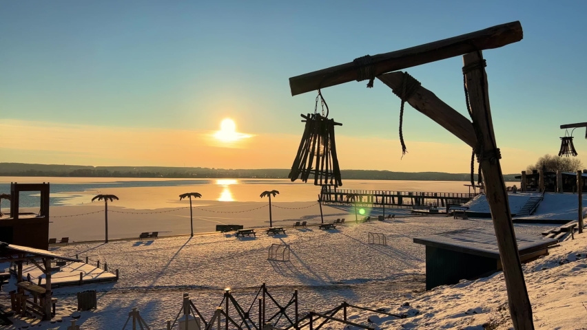 A lantern on the background of an orange sunset over a pond. A huge sun over the pond. The cold clear water is covered with the first snow and thin ice. Russia