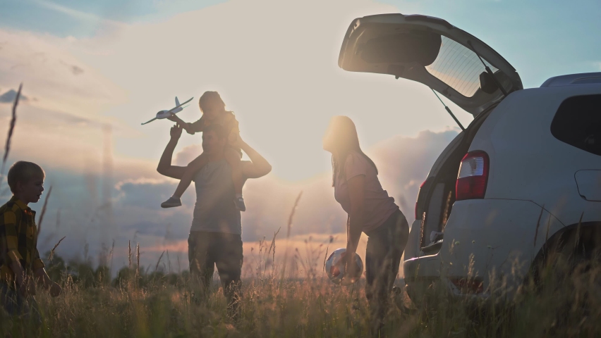 happy family children stand together next to the car watching the sunset silhouette in the park. family travel dream concept. happy family standing, back watching sunlight the journey in the park