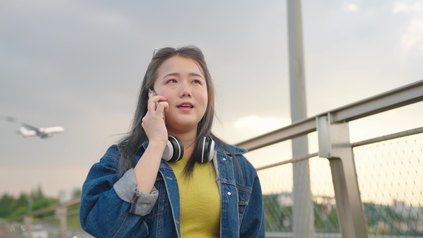 Happy asian woman smilling face talking with smartphone looking the watch on the wrist at outdoor. Background sky and airplane