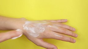 Young woman applying moisturizing cream on her hand. Skin care concept video. Isolated on yellow chroma key background.
