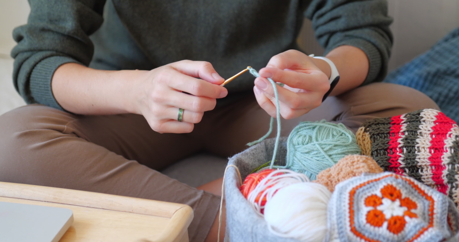 Close-up video of woman learning to crochet. Felt basket with balls of yarn. Anti-stress hobby. Online lessons for amateurs on laptop.