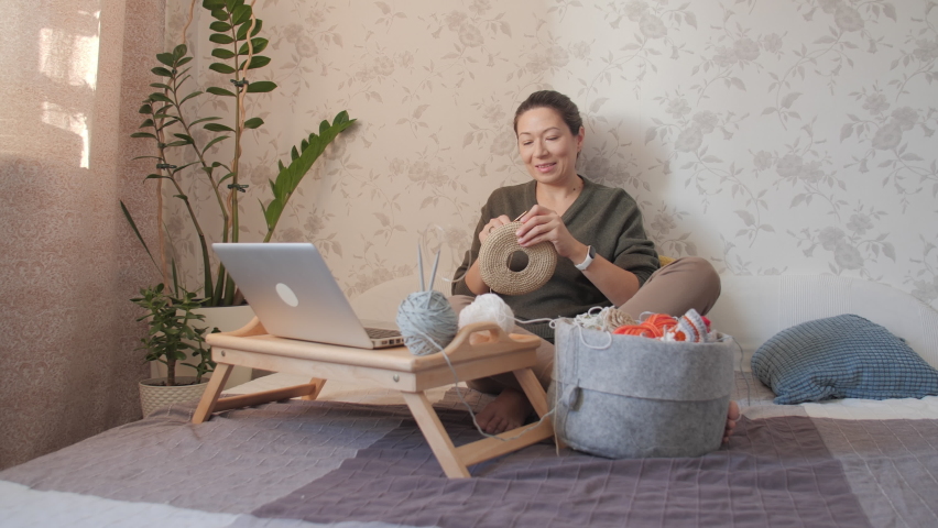 Close-up video of woman learning to crochet. Felt basket with balls of yarn. Anti-stress hobby. Online lessons for amateurs on laptop.