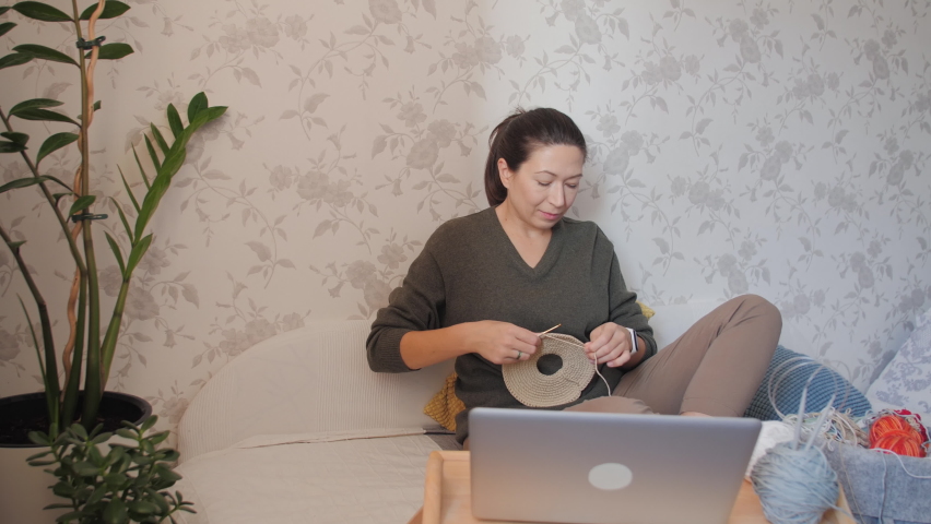 Close-up video of woman learning to crochet. Felt basket with balls of yarn. Anti-stress hobby. Online lessons for amateurs on laptop.