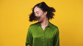 Beautiful fun fancy smiling happy young woman of Asian ethnicity 20s she wear green shirt dance waving fooling around have fun enjoy play fluttering hair isolated on plain yellow color wall background - Powered by Shutterstock - Get 15% off with code: PIKWIZARD15