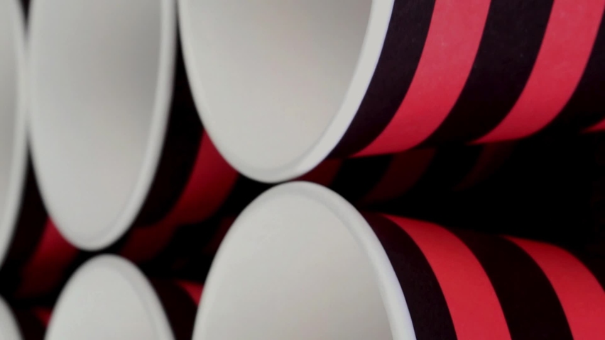 Row red and black disposable paper cup for coffee or hot beverage on dark backdrop rotate slowly.