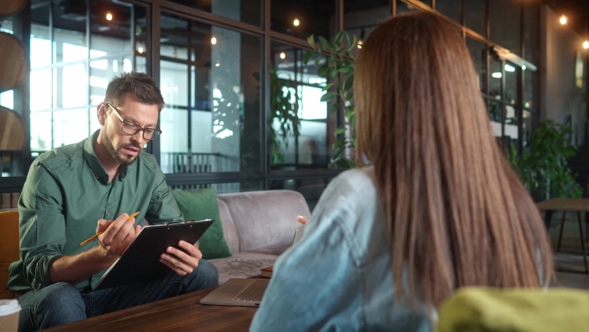 Young elegant successful businessman interviewing pretty beautiful woman on job interview in cafe. Handsome bearded man making notes and long-haired female sitting on chair. Job interview concept. Royalty-Free Stock Footage #1097047873