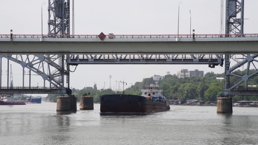 Side view of black deck of large oil lighter sailing under open train lift bridge in city. Real time video. Shipping theme. | Shutterstock HD Video #1097058413