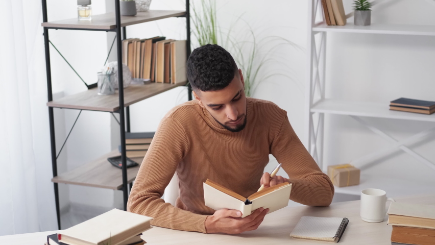 Home education. Male student. Preparing lecture. Concentrated casual man turning pages of book sitting desk in light room interior.