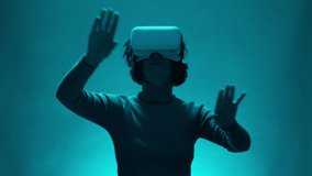 Mature Woman 40s Using Virtual Reality Headset In Studio on blue background. Adult Model Making Gestures to Reviewing Business Documents or Answering to Email Colleague.Modern Female on Online Meeting - Powered by Shutterstock - Get 15% off with code: PIKWIZARD15