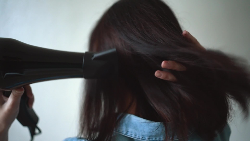 The girl dries her hair with a hairdryer. Concept of well-groomed and beautiful woman. Close up video of Woman drying hair using black hair dryer. Royalty-Free Stock Footage #1097061593