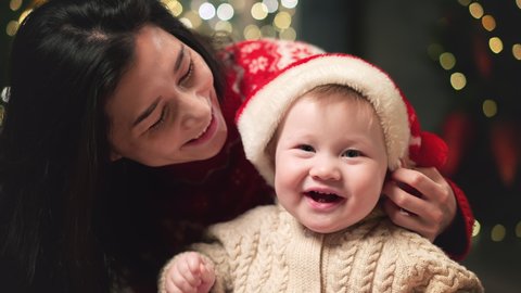 Mom puts a red Christmas hat on her baby. Family Spending Winter Evening at Home. Young Mother with Little Kid Son play. Slow Motion. Christmas, New Year, Winter Christmas Holiday Celebration. Stock Video