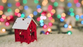 Red wooden house with deer on the background of Christmas lights. Place to copy. New Year multi-colored lights in defocus. Beautiful holiday card, video for intro, text, intro. UHD 4K.