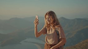 School-age child makes video call to friends while hiking in mountains. Teenage girl smiling while talking over video call