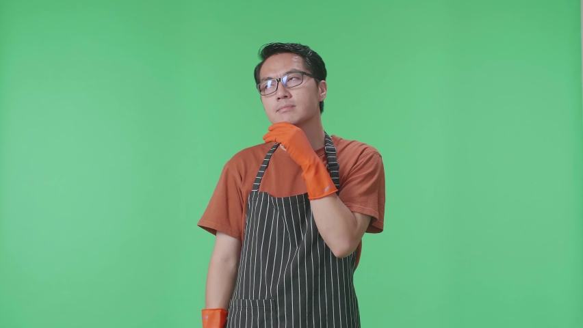 Asian Male Housekeeper With An Apron Thinking About Something And Looking Around While Standing In The Green Screen Studio
 | Shutterstock HD Video #1097077575