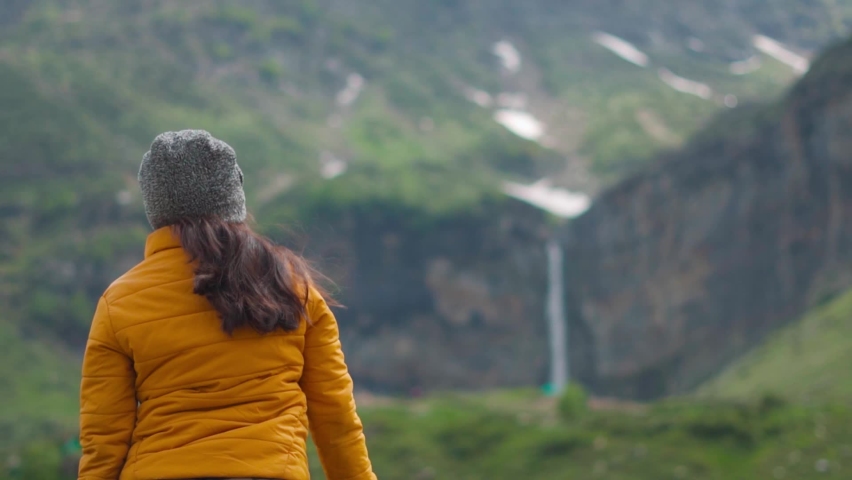 Rack focus shot of Sissu waterfall with a female Indian tourist standing in front of it at Lahaul and Spiti district, Himachal pradesh, India. Focus changes from girl traveler towaterfall.  | Shutterstock HD Video #1097078141