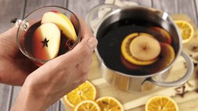 Woman's hands holding a glass mug with mulled wine, closeup 4k video, Christmas punch, festive alcohol drink, scented red hot wine with cinnamon, orange, apple fruit and spice, hd footage