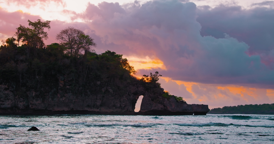 Ocean sunset static view from Crystal Bay beach on small island Nusa Penida Bali Indonesia. Close-up to splashing sea waves, rock sticking out of water with hole inside.