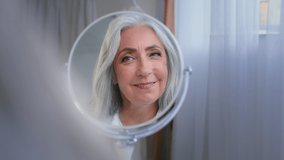 Female reflection in mirror at home pampering old lady Caucasian 60s middle-aged mature Caucasian woman 50s female looking on herself smile wrinkled face skin care gray haircare moisturizing aging - Powered by Shutterstock - Get 15% off with code: PIKWIZARD15