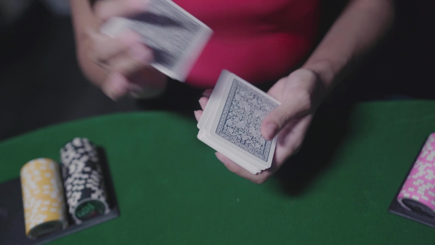 Young woman shuffles a deck of cards for a poker game. There are poker chips of different denominations on the table.